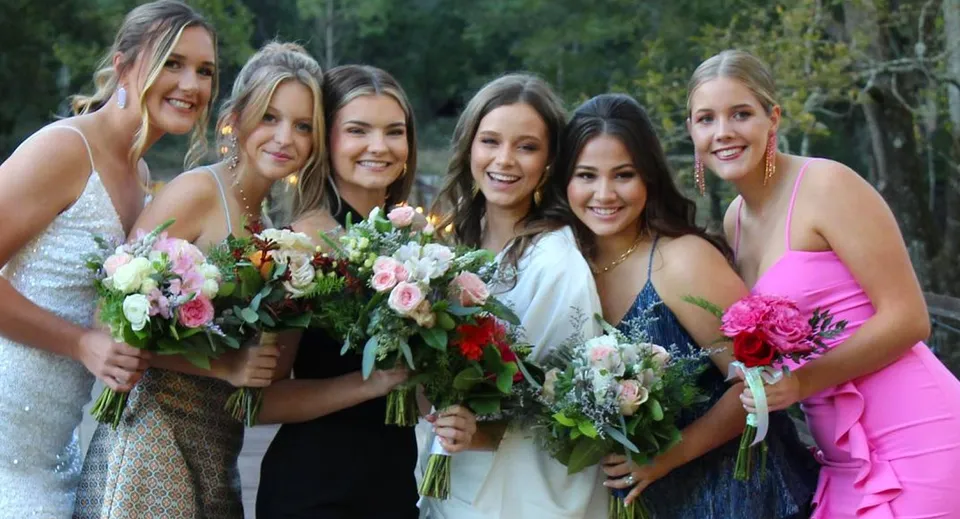 Un gruppo di studentesse sorridenti della Darlington School si trova in un'area verde all'aperto con mazzi di fiori.