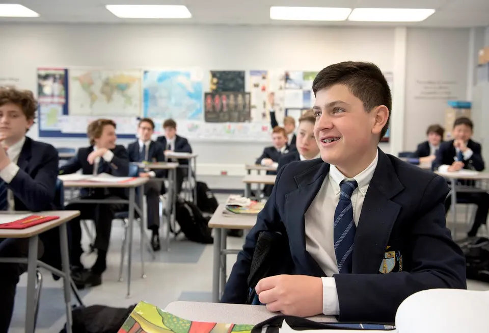 Uno studente della St. Michael's School in divisa scolastica sorride seduto al suo banco in classe.