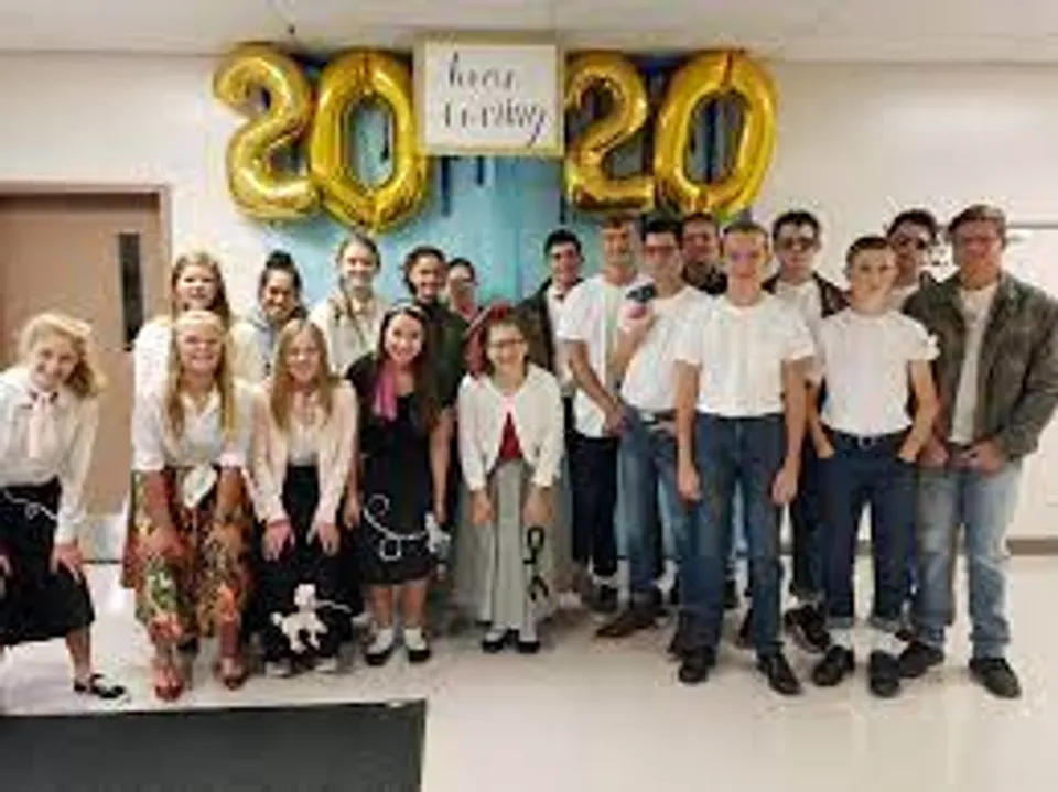 Un gruppo di studenti e studentesse si trova in una stanza con grandi palloncini dorati sullo sfondo nel campus della Nebraska Christian Schools.