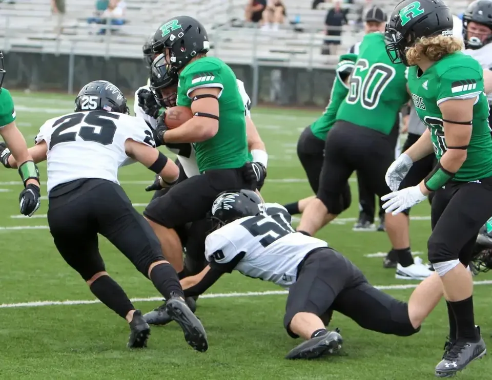 Giocatori di football americano della Regis High School in maglia verde durante una partita.