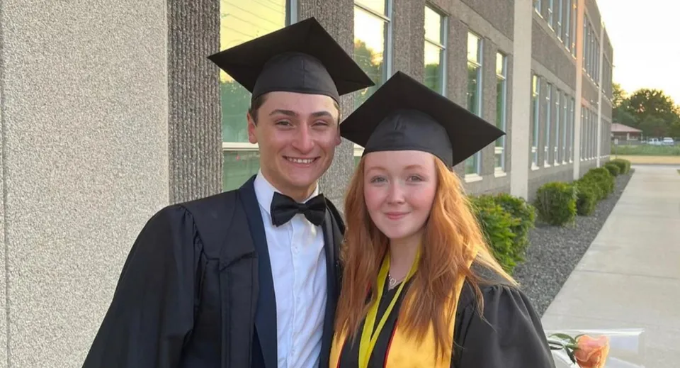 Due diplomati sono davanti a un edificio della Leamington District Secondary School con toghe da diploma e mortarboard.