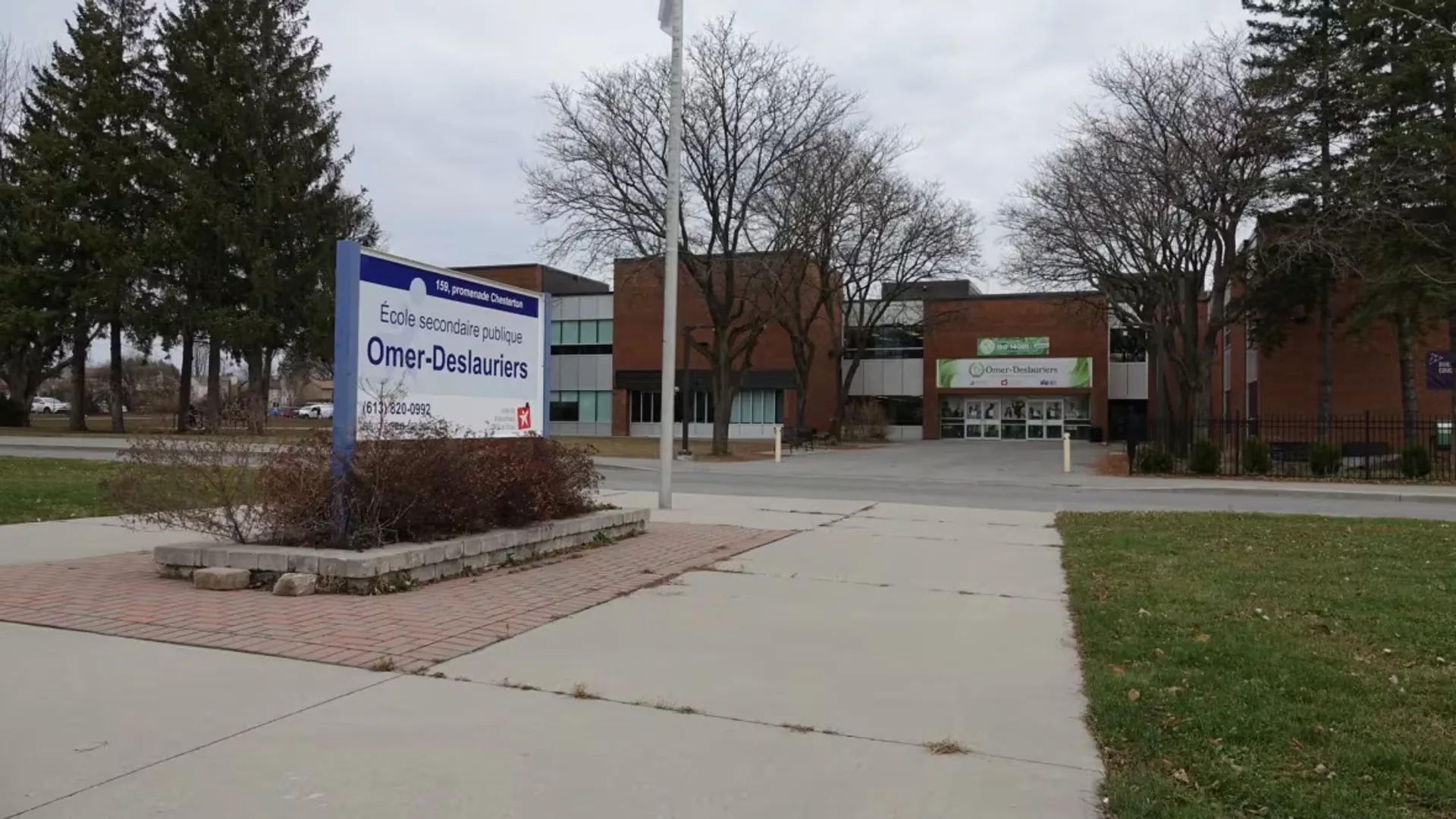 Un vialetto conduce a un edificio in mattoni con il cartello 'Crime-Disasters' nel campus della École secondaire publique Omer-Deslauriers.