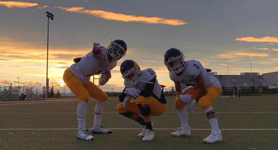 Tre giocatori di football americano in divisa si preparano sul campo da gioco della Ernest Manning High School.