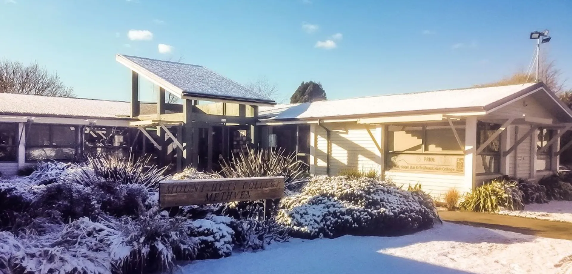 Una casa in legno innevata con pannelli solari sul tetto si trova nel campus del Mount Hutt College, circondata da una rigogliosa vegetazione.