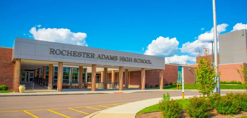 Il grande edificio in mattoni delle Rochester Community Schools sotto un cielo blu con nuvole bianche.