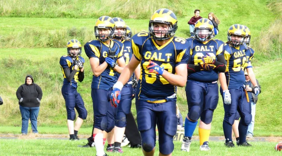 Un gruppo di giovani calciatori sta sul campo in erba della Alexander Galt Regional High School.