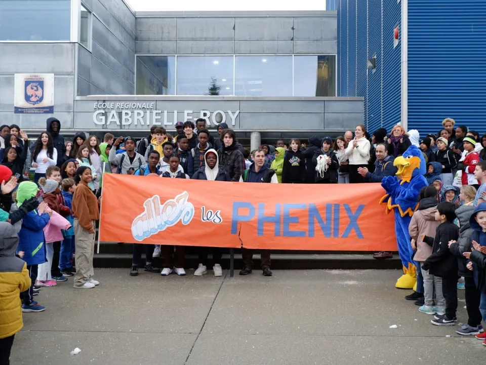 Studenti della École Gabrielle-Roy tengono un grande striscione arancione con la scritta Los Phenix davanti all'edificio scolastico.