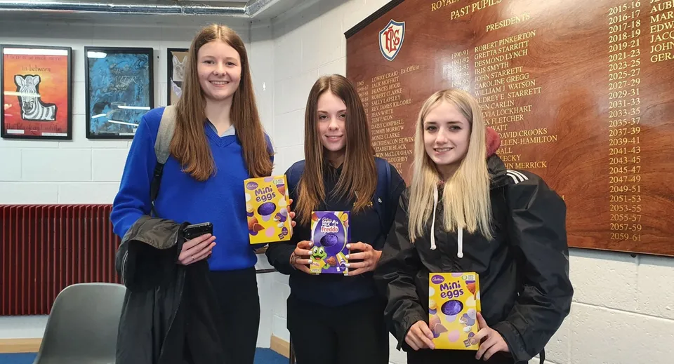 Tre studentesse sono insieme nel corridoio della Royal & Prior Comprehensive School con dei libri in mano.