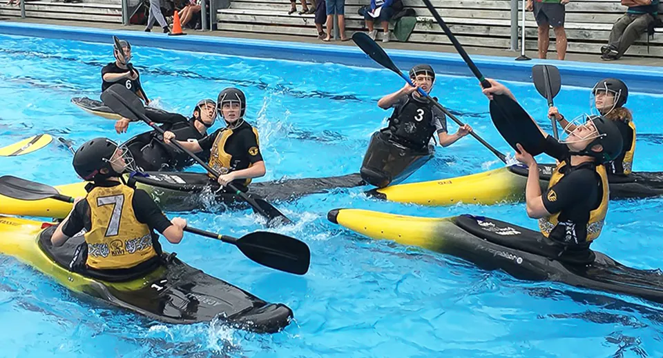 Diversi giocatori di kayak polo dell'Awatapu College pagaiano con il casco in piscina.