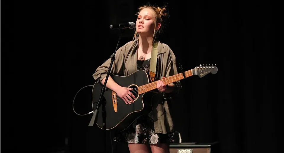 Una studentessa della Wasatch Academy suona la chitarra acustica sul palco e canta in un microfono.