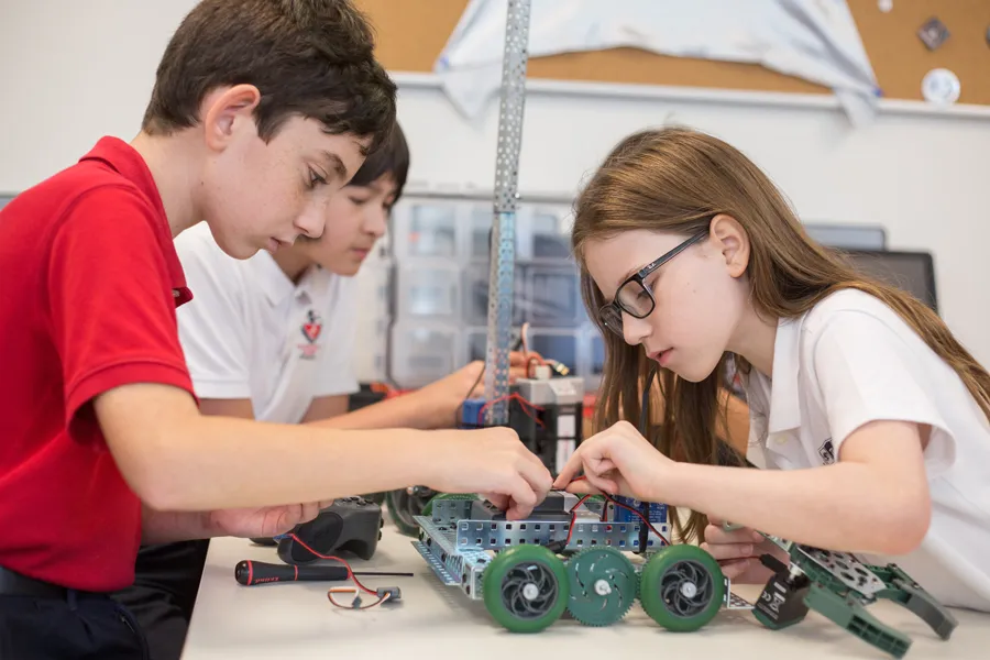 Tres estudiantes de la Fulton Science Academy trabajan juntos en la construcción de un robot con ruedas verdes.