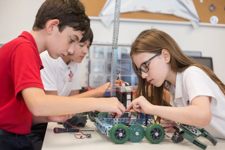 Tre studenti della Fulton Science Academy lavorano insieme alla costruzione di un robot con ruote verdi.