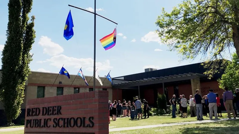 Un gruppo di persone si trova davanti all'edificio delle Red Deer Public Schools con bandiere issate.