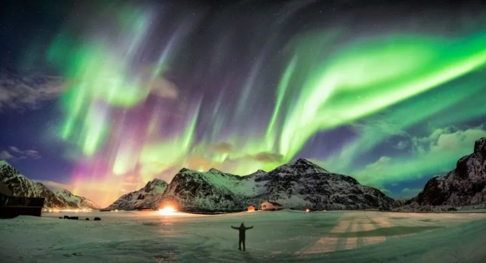 L'aurora boreale illumina il cielo notturno sopra un paesaggio innevato con una capanna e una persona davanti alla Brookfield High School.
