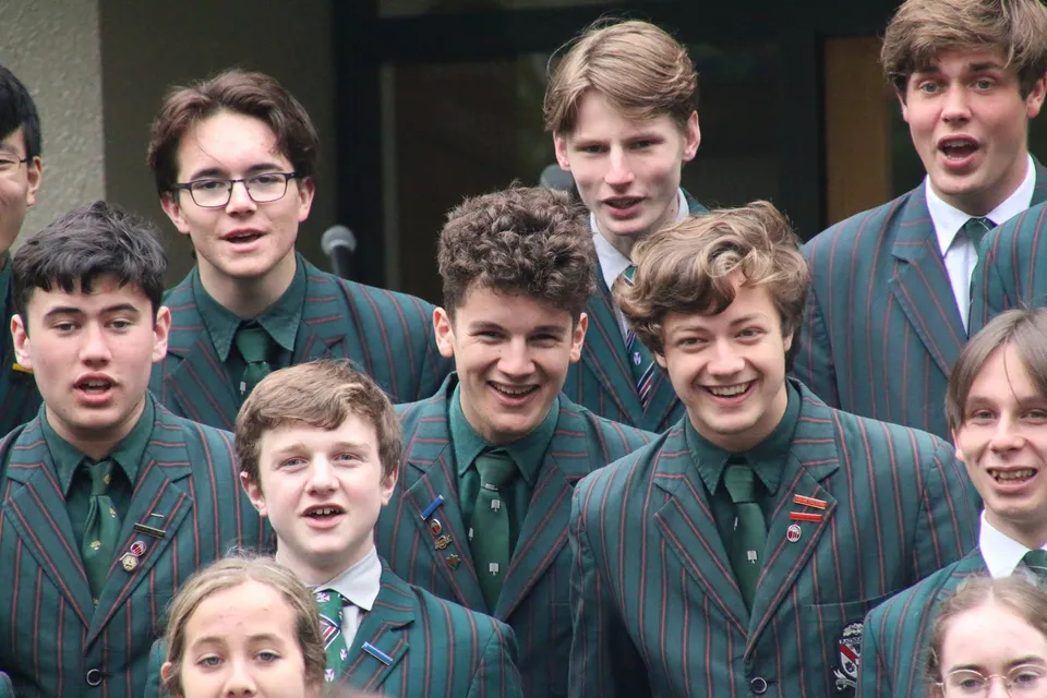 Un gruppo di studenti in uniforme verde mostra espressioni facciali espressive nel campus del Rathkeale College.