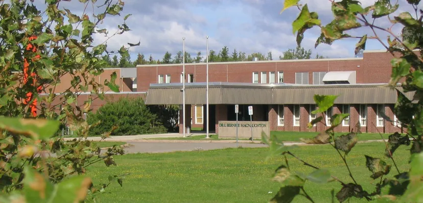 L'edificio in mattoni con ingresso coperto nel campus della Bernice McNaughton High School è circondato da alberi e prato.