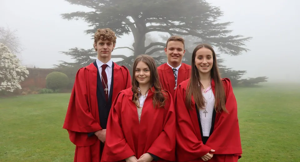 Un gruppo di quattro diplomati in toga rossa si trova su un prato nel campus dell'Ashville College.