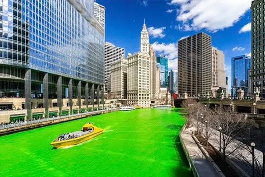 Barco amarillo navegando por un río teñido de verde rodeado de grandes rascacielos urbanos