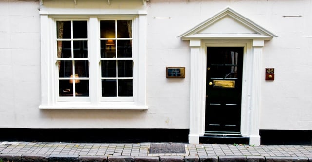 Un edificio bianco con una porta in legno nera e una grande finestra nel campus del Greene's College Oxford.