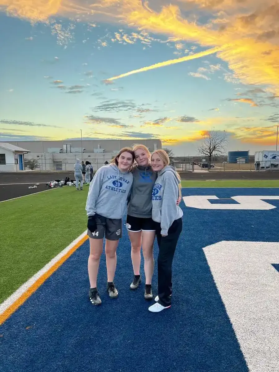 Tre studentesse in felpa sportiva su un campo da gioco al tramonto