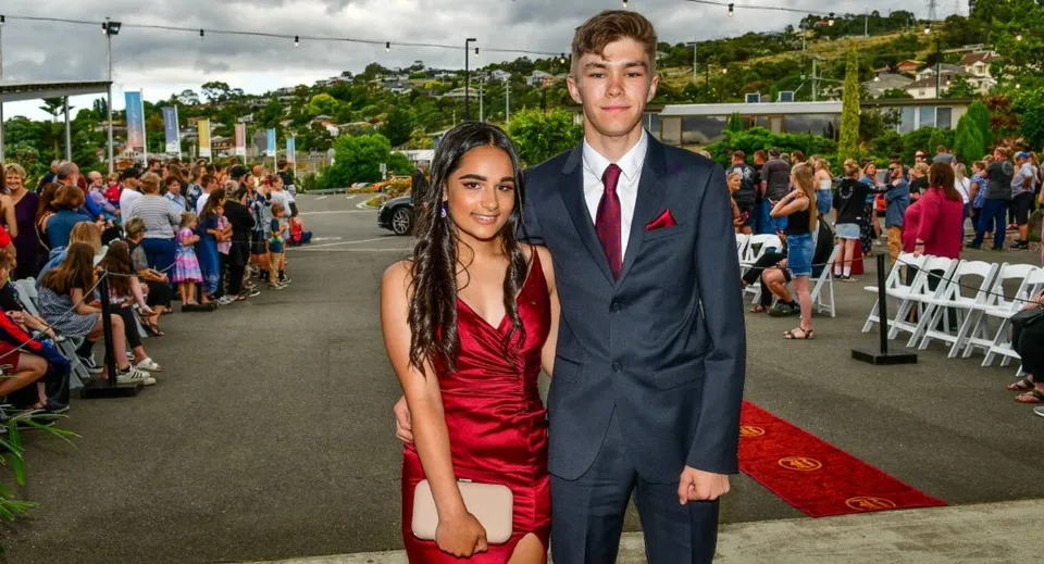 Studenti della Queechy High School posano in abito formale sul tappeto rosso davanti a una folla.