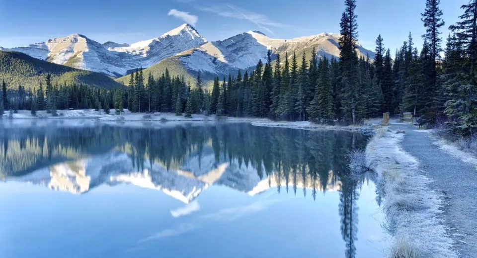 Un lago calmo riflette montagne innevate e una foresta di conifere nei dintorni della Elphinstone Secondary School.