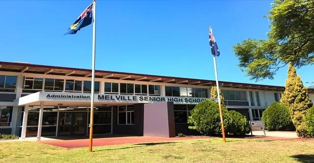 Der Haupteingang der Melville Senior High School mit australischer und Western Australian Flagge im Vordergrund und Bäumen im Hintergrund.