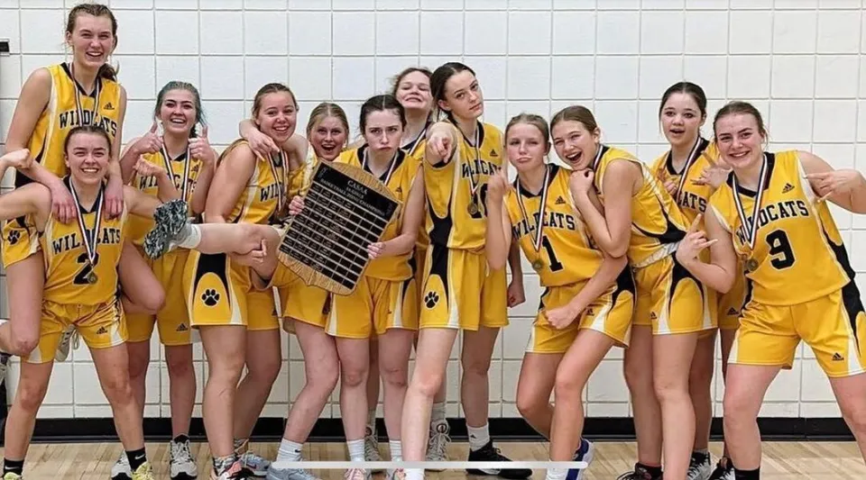 Un gruppo di giovani giocatrici di pallacanestro in maglia gialla posa alla Bawlf School davanti a una parete piastrellata.