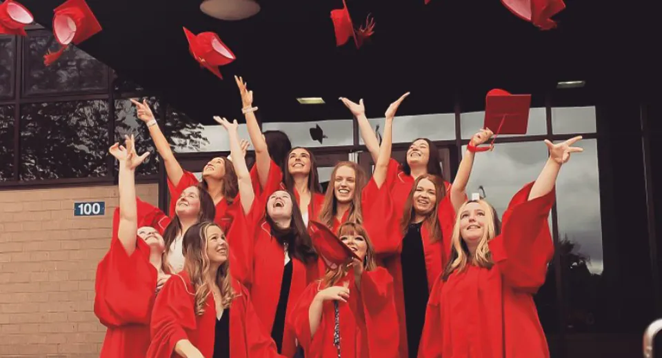 Studentesse della Charlottetown Rural High School alzano le braccia nelle loro toghe rosse durante un'esibizione sul palco.