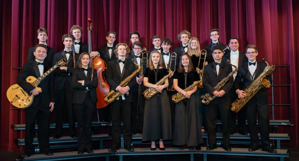 Un gruppo di musicisti sta sul palco con tende rosse e tiene vari strumenti presso la Scoil Mhuire gan Smál.