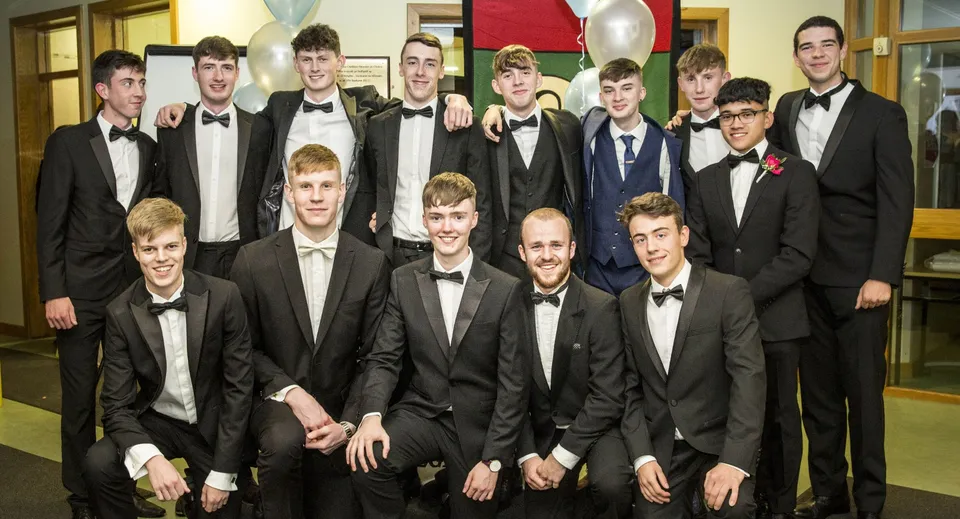 Un gruppo di giovani uomini in abito formale posa nel corridoio dell'Oatlands College con decorazioni e palloncini sullo sfondo.