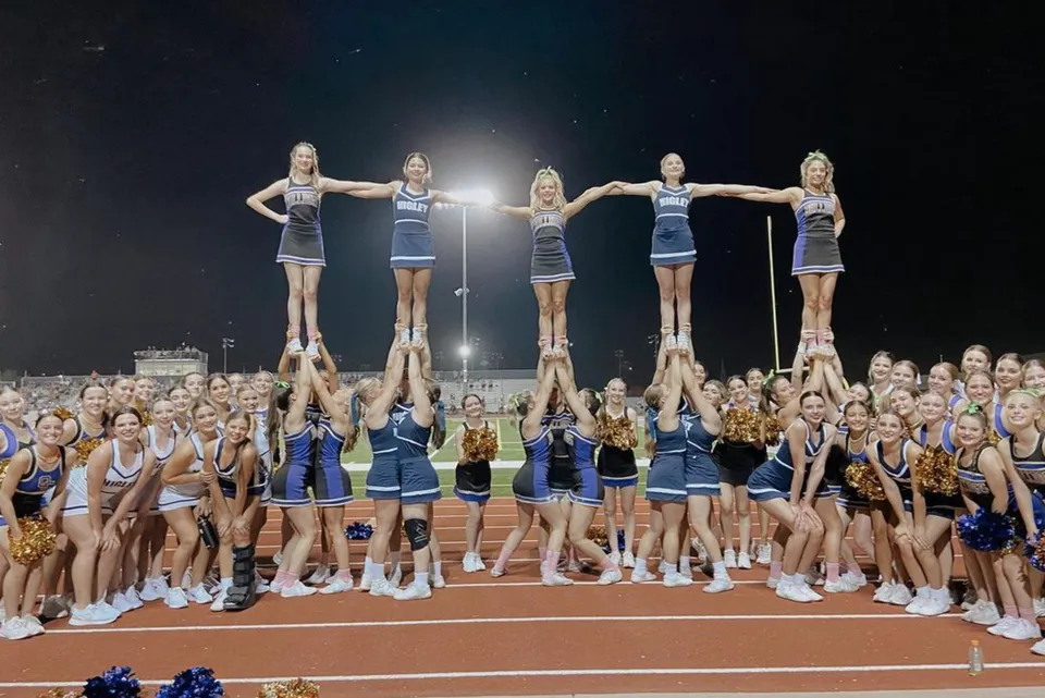 Le studentesse della Higley High School eseguono uno stunt da cheerleader sul campo sportivo davanti a un grande pubblico.