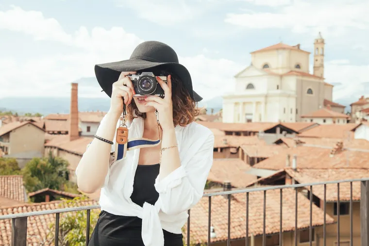 Frau mit schwarzem Hut fotografiert mit einer Kamera über den Dächern einer Altstadt