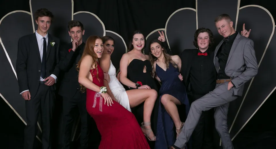 Un gruppo di persone in abito formale posa davanti a uno sfondo astratto nel campus della Taradale High School.
