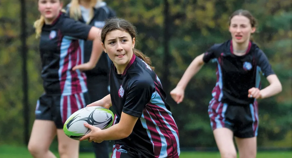 Studentesse della The Bishop Strachan School giocano a calcio su un campo in erba con alberi sullo sfondo.