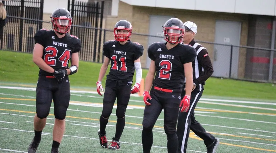 Un gruppo di giovani calciatori si trova sul campo da gioco della Our Lady of the Rockies High School davanti a un edificio scolastico.