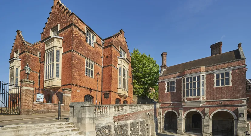 L'edificio principale storico della Harrow School con dettagli artistici, circondato da una verde vegetazione sotto un cielo limpido.