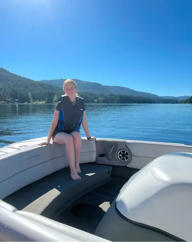 Studentessa con giubbotto di salvataggio seduta su una barca su un lago tra le montagne boscose