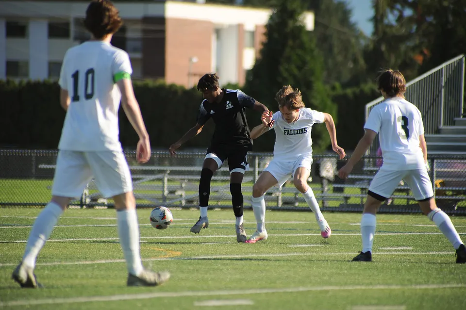 Un gruppo di studenti gioca a calcio sul campo verde della Abbotsford Senior Secondary School, con edifici e alberi sullo sfondo.