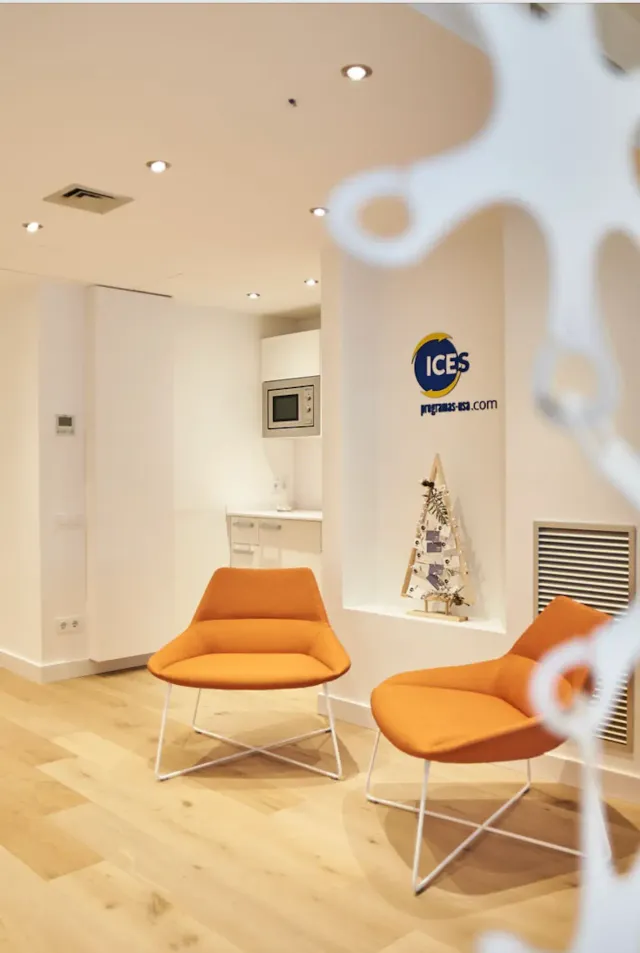 Sala de espera de la oficina de ICES con dos butacas naranjas y el logotipo en la pared