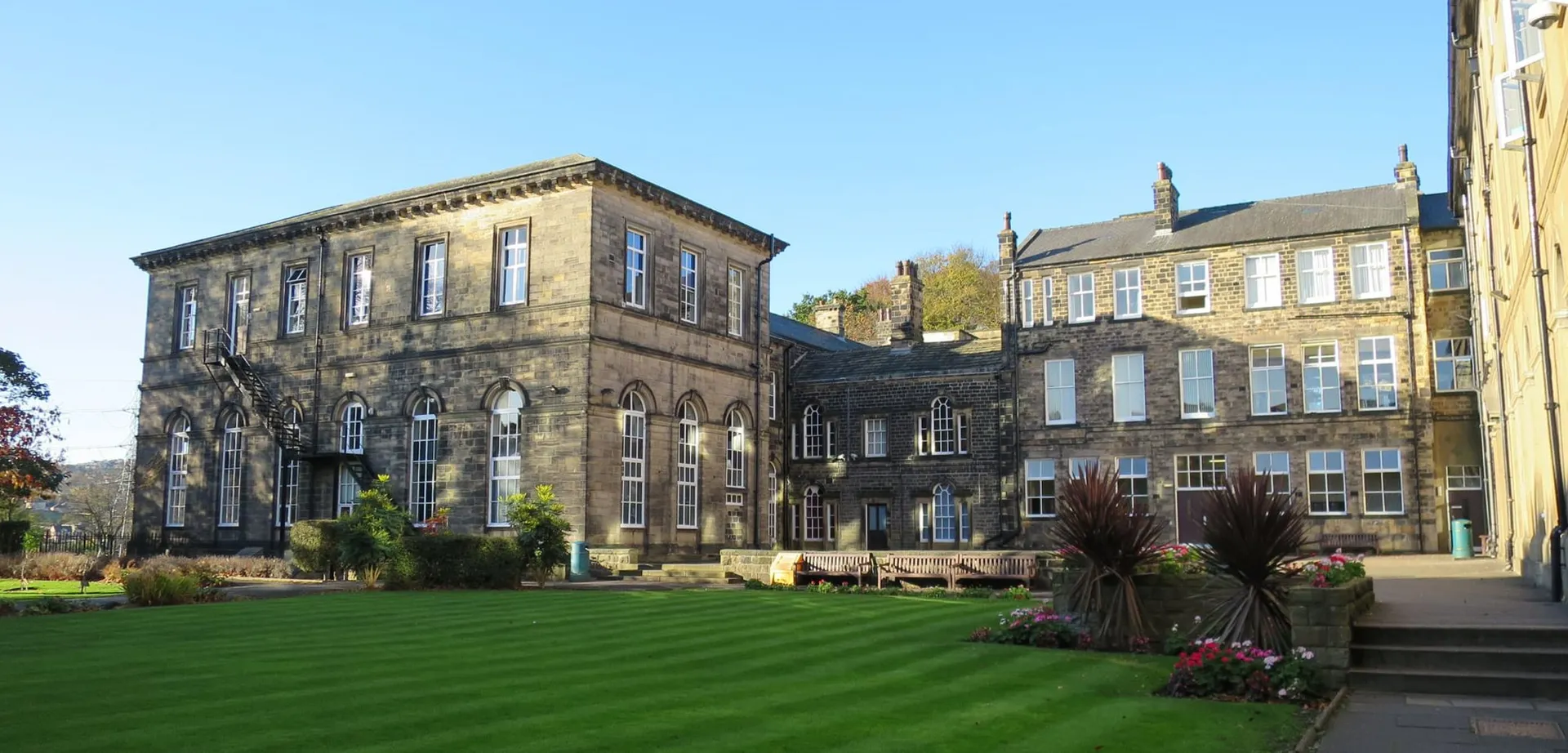 L'edificio principale storico della Woodhouse Grove School con un prato ben curato e aiuole fiorite in primo piano.