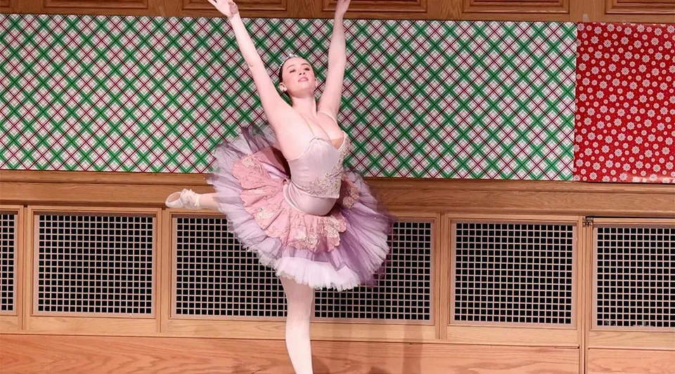 Una ballerina in tutù e body rosa esegue un'elegante posa di danza davanti a uno sfondo colorato alla St. Andrew's School.