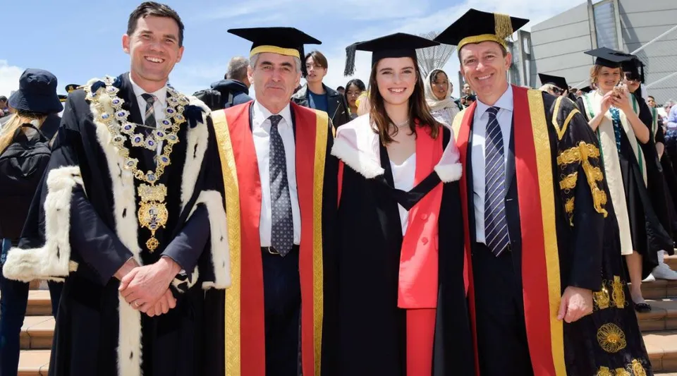 Un gruppo di studenti della Victoria University of Wellington in toga di laurea posa davanti a un edificio universitario.