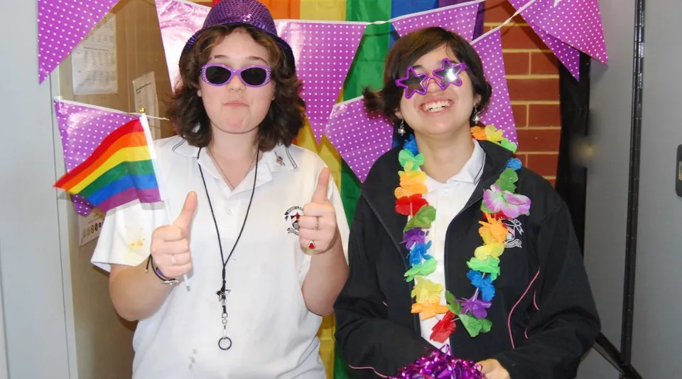 Due studentesse della Mount Lawley Senior High School posano davanti a uno sfondo decorato con vivaci bandiere arcobaleno.