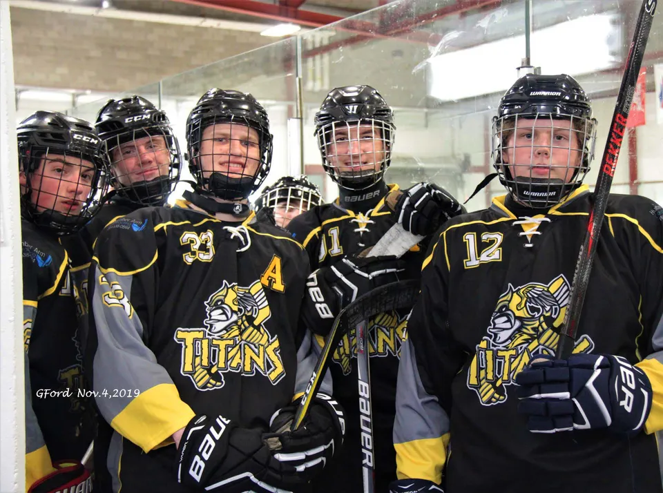 Un gruppo di giovani giocatori di hockey della Corner Brook Regional High School si trova nello spogliatoio con le maglie da gioco e i caschi.