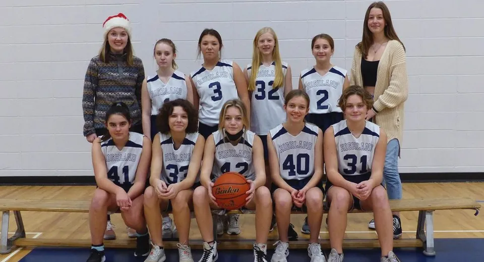 Un gruppo di giovani giocatrici di basket della Highland Secondary School posa insieme in palestra con un pallone da basket.