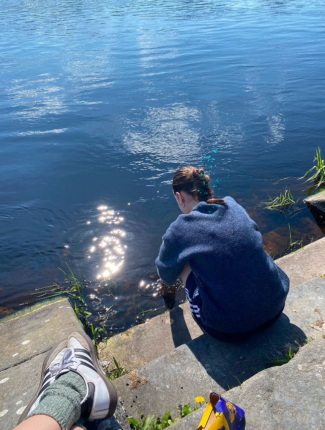 Estudiante sentada en unas escaleras de piedra junto al río en un día soleado