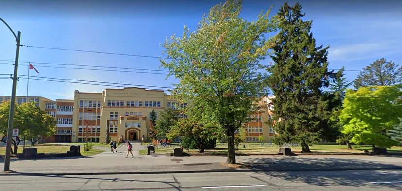 Il campus della Vancouver Technical Secondary School mostra grandi alberi davanti a edifici scolastici a più piani sotto un cielo limpido.