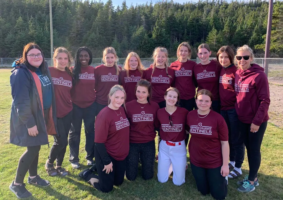 Un gruppo di studentesse della Carbonear Collegiate High School si trova su un campo erboso circondato da alberi.