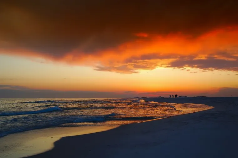 Leuchtend orangefarbener Sonnenuntergang über einem Strand mit Spaziergängern in der Ferne